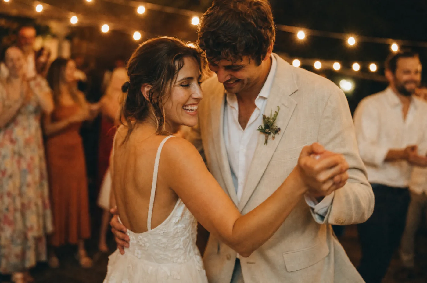 Couple dancing their first dance under string lights, gentle motion blur
