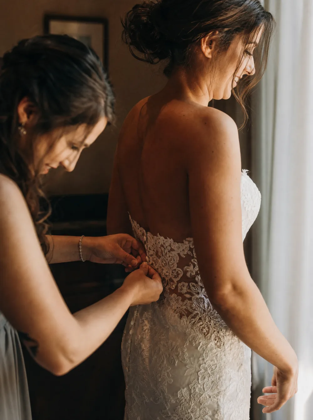Bride getting ready in soft window light, candid focus on hands and dress details